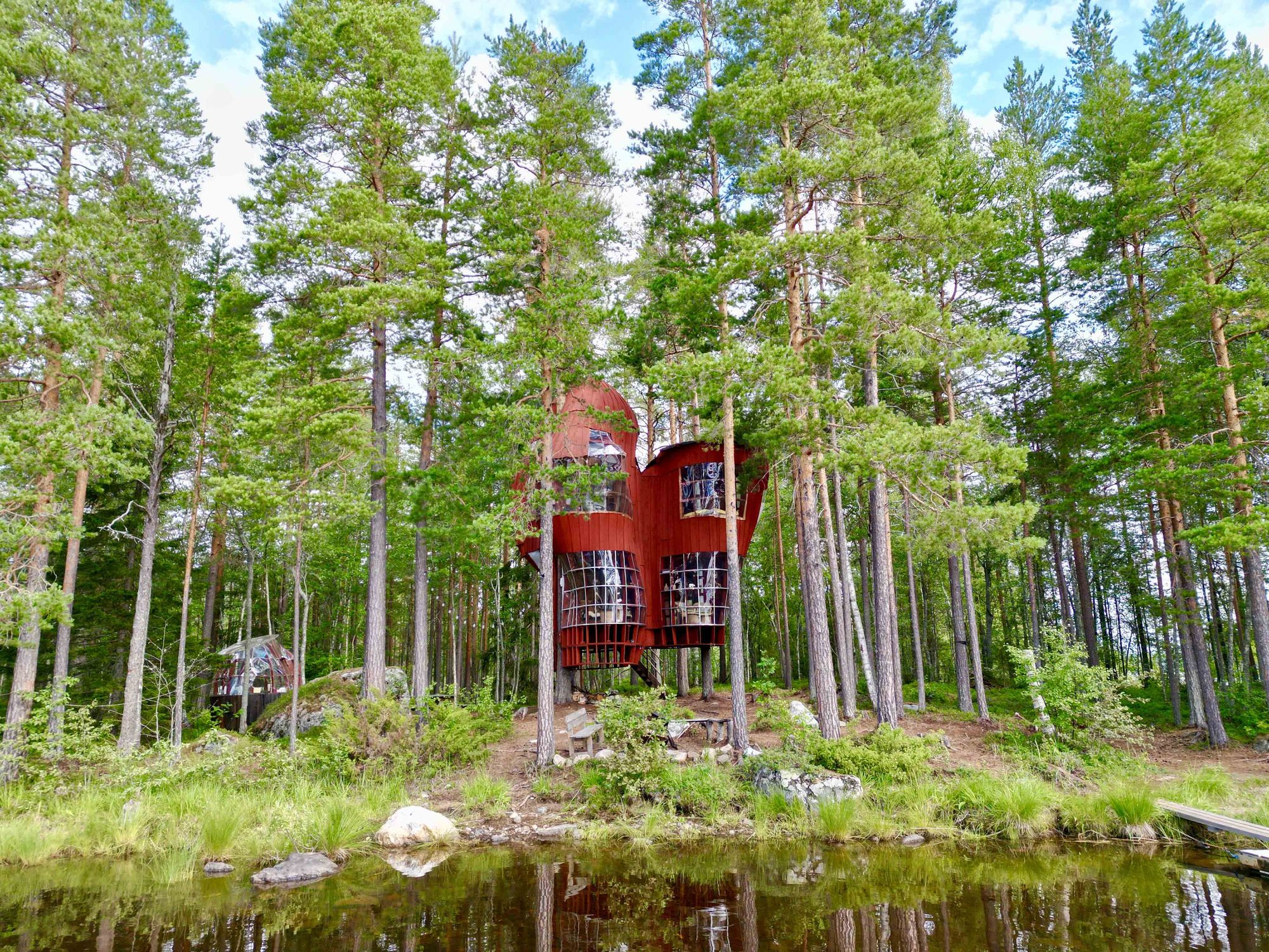 Foto på trähus mellan träd framför en sjö