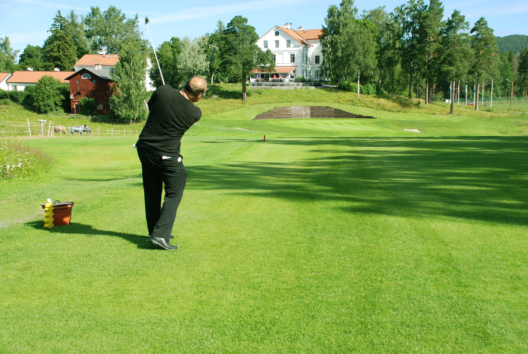 En man i svarta kläder står och chippar in på en green.