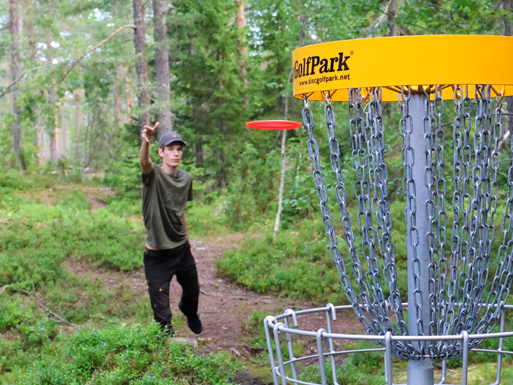 Bilden visar en discgolfspelare som puttar emot korg nummer 2 på Södra Berget discgolfbana i Sundsvall.