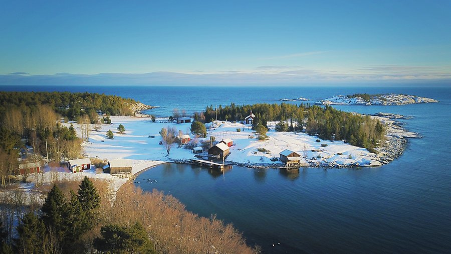 Drönarfoto över snöigt kustlandskap med gamla sjöbodar och klippor